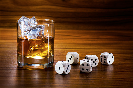 whiskey with ice and dice on a warm toned wooden table, concept of addiction, copy space